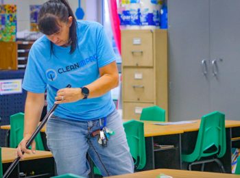 Cleaning professional in Clean Impact LLC uniform meticulously cleaning a classroom, showcasing dedication to high standards of service and personal excellence.